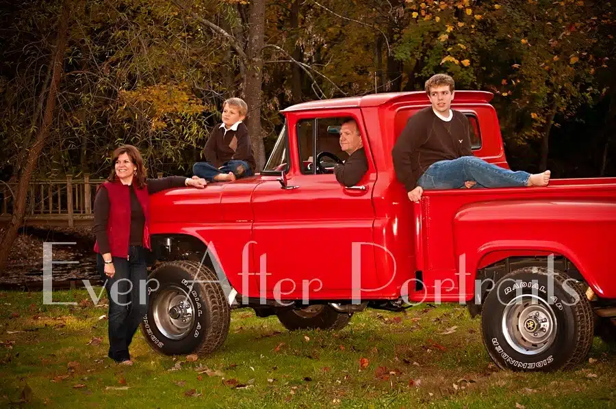 Family posing by red truck in autumn.